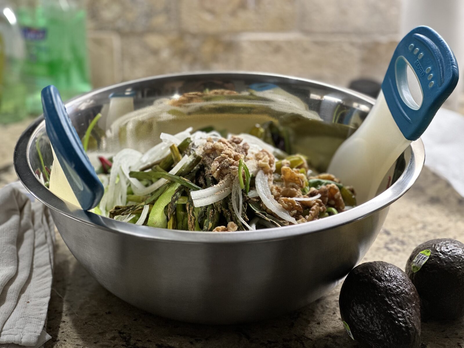 A stainless steel bowl of roasted asparagus tossed with thinly sliced onion and toasted walnuts