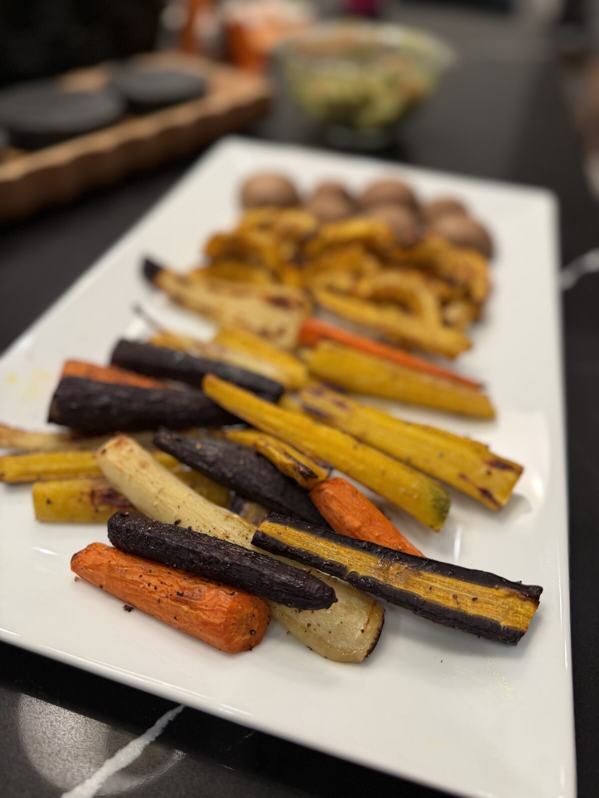 A long white platter of caramelized rainbow carrots and delicata squash